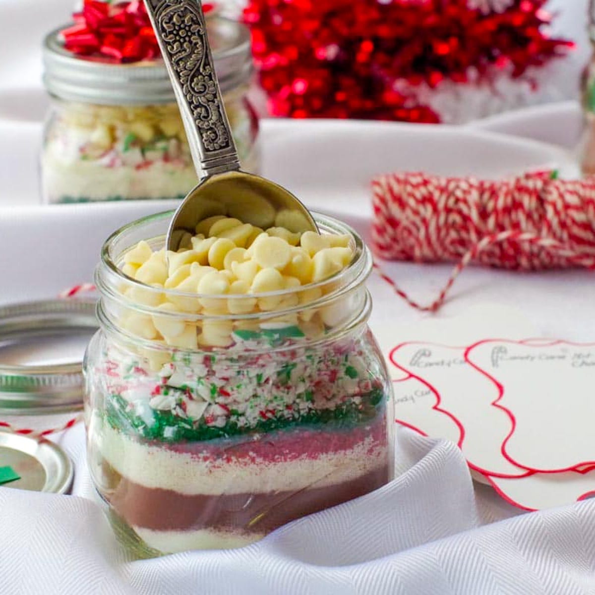 White chocolate holiday layered dessert in a mason jar with festive decorations and handwritten recipe tags for Christmas treats.
