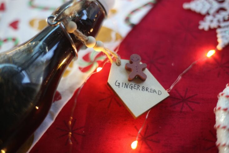 Delicious gingerbread cookie tied to a jar of homemade gingerbread syrup with festive holiday decorations and fairy lights, perfect for Christmas treats and seasonal baking.