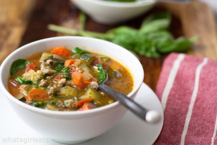 Hearty homemade vegetable soup with fresh carrots, zucchini, spinach, and ground meat in a flavorful broth, served in a white bowl on a rustic wooden table.