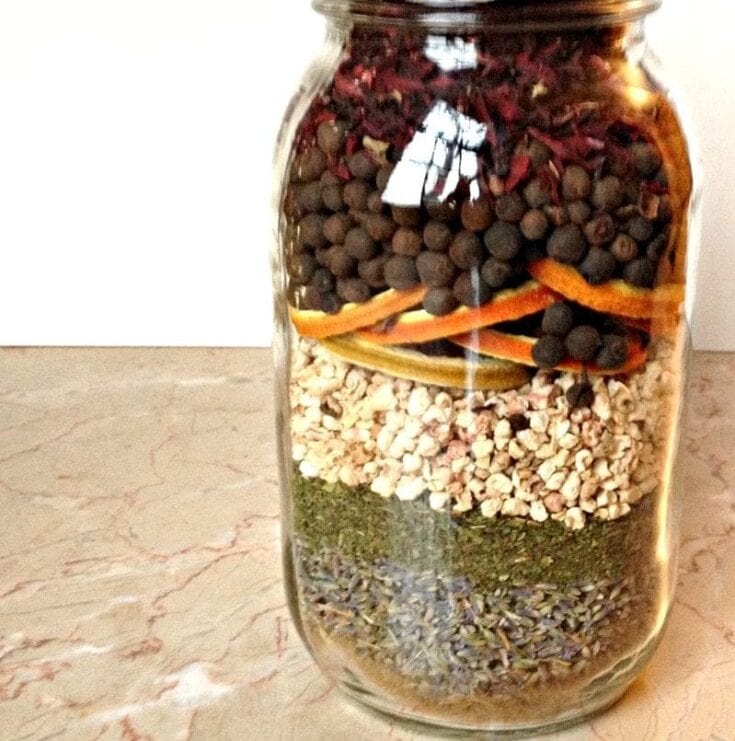 Organic herbal tea blend in a glass jar with layers of dried herbs, spices, dried fruit, and flowers for natural wellness and aromatic brewing.