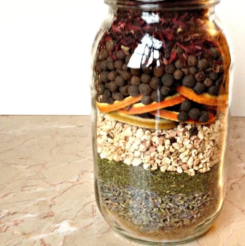 Organic herbal tea blend in a glass jar with layers of dried herbs, spices, dried fruit, and flowers for natural wellness and aromatic brewing.