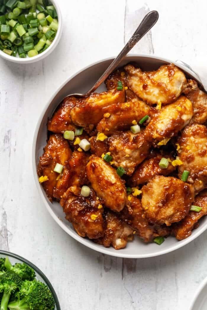 Savory honey garlic chicken wings garnished with green onions and lemon zest on a white plate, perfect for easy appetizers or party snacks.