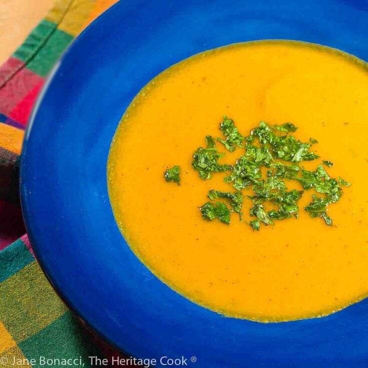 Creamy butternut squash soup garnished with fresh chopped parsley in a vibrant blue bowl on a colorful checkered cloth.