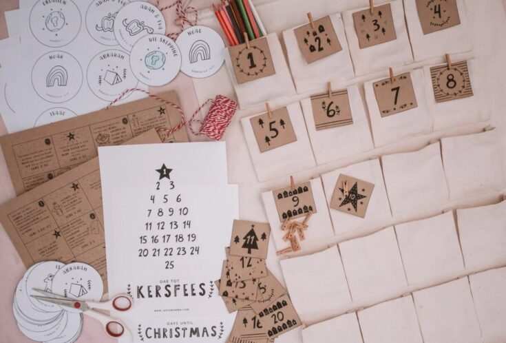 A festive Advent calendar craft kit with numbered paper envelopes, wooden clothespins, decorative tags, and holiday-themed embellishments for Christmas counting and activity tracking.