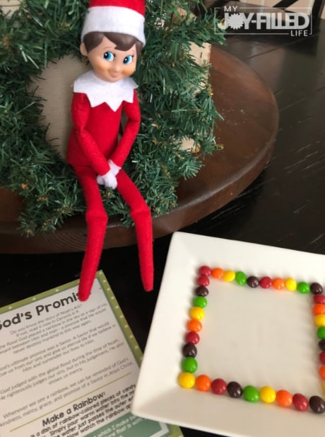 Cute Christmas Elf doll with a red hat and outfit sitting next to a decorated Christmas table and a colorful candy bead frame, perfect for holiday decor and festive celebrations.