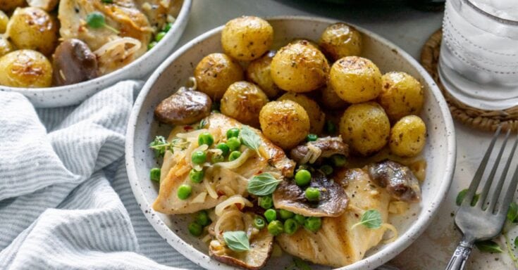 Golden roasted baby potatoes with fresh herbs, served alongside a comforting chicken and mushroom casserole with peas, in a rustic setting for a cozy home-cooked meal.