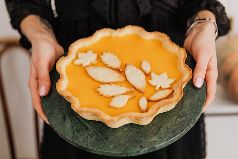 Golden lemon tart with a decorative white leaf pattern on top, presented on a dark green marble plate, showcasing elegant dessert artistry and fresh homemade baking.