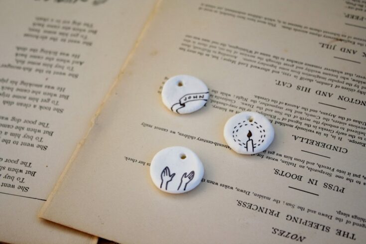 Handmade ceramic tags with delicate line drawings of a candle, hands, and a name banner, laid on vintage paper, perfect for personalized gift tags, jewelry, or decorative accents in a cozy, heartfelt setting.
