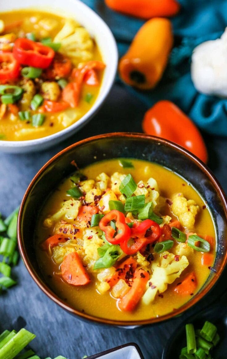 Creamy vegetable soup with cauliflower, carrots, and red peppers garnished with chopped green onions, served in rustic bowls, perfect for cozy, healthy meals.