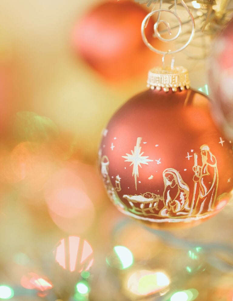 Ornament featuring a snowy nativity scene with Mary, Joseph, and baby Jesus on a Christmas tree, illuminated by festive lights, celebrating holiday traditions and seasonal decor.