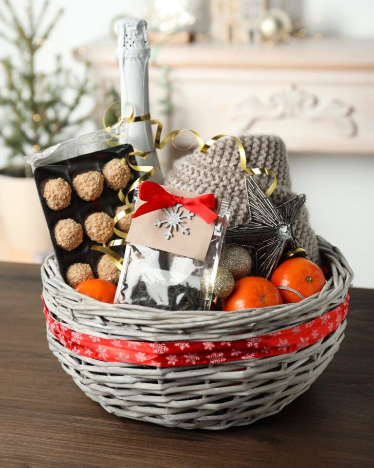 Festive holiday gift basket with chocolates, oranges, holiday ornaments, a bottle of champagne, cozy sweater, and Christmas decorations, perfect for Christmas celebrations and gift-giving.