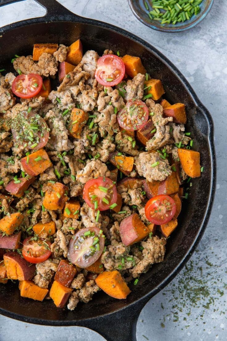Sautéed ground meat with sweet potatoes and cherry tomatoes in a cast iron skillet, garnished with chopped green onions and herbs, perfect for easy weeknight dinners.