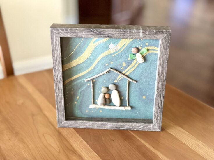 Miniature nativity scene artwork crafted with small stones and delicate details, framed in a rustic wooden shadow box, perfect for holiday home decor and meaningful Christmas crafts.