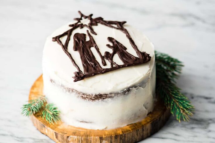 Deluxe Christmas cake with nativity scene chocolate topper on a rustic wooden base, decorated with pine sprigs, perfect for holiday celebrations and festive gatherings.