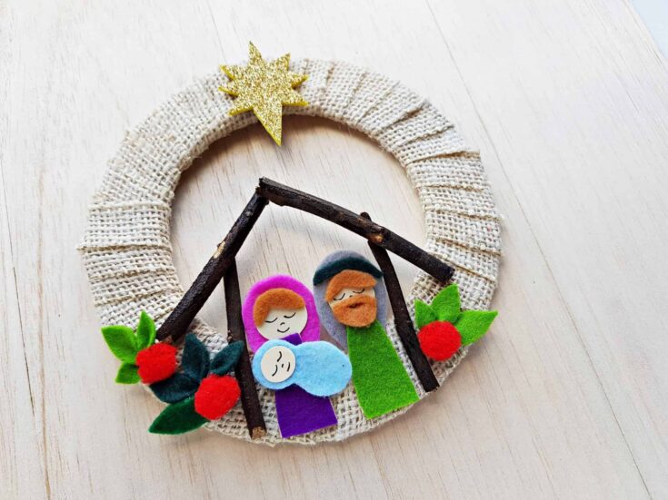 Felt nativity scene with Mary, Joseph, and baby Jesus on a rustic wreath with holly accents, perfect for Christmas decoration.