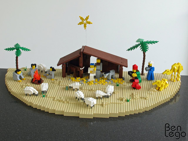 Lego nativity scene with traditional figures, palm trees, and animals on a sandy base, representing a scenic Christmas biblical story.