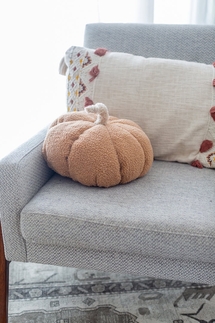 Soft plush pumpkin cushion on light gray sofa with decorative pillows, cozy autumn home decor, seasonal pumpkin accent, comfortable living room decor, fall decor ideas.