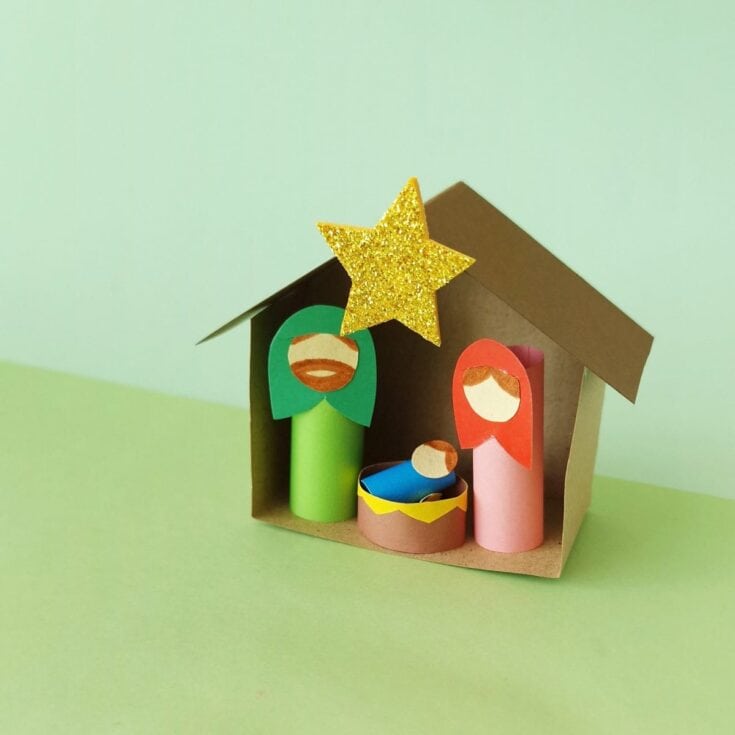 Colorful handmade paper nativity scene featuring paper tube figures of Mary, Joseph, baby Jesus, and a glittery gold star at the top, made with craft paper and simple materials for holiday decor.