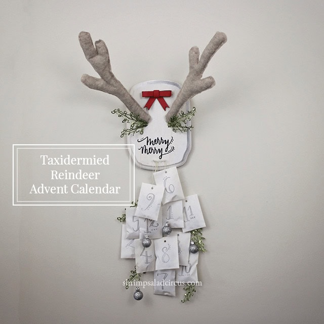 Cozy taxidermied reindeer advent calendar with soft faux antlers, festive red bow, greenery, and numbered envelopes, perfect for holiday home decor and Christmas countdowns.