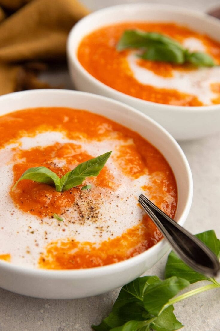 Rich tomato soup with creamy swirl and fresh basil garnish, served in white bowls, showcasing comforting homemade recipes from A Hundred Affections.