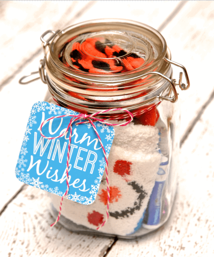 A glass jar with a colorful sock inside and a "Warm Winter Wishes" tag attached, perfect for winter gift-giving or cozy holiday decor.