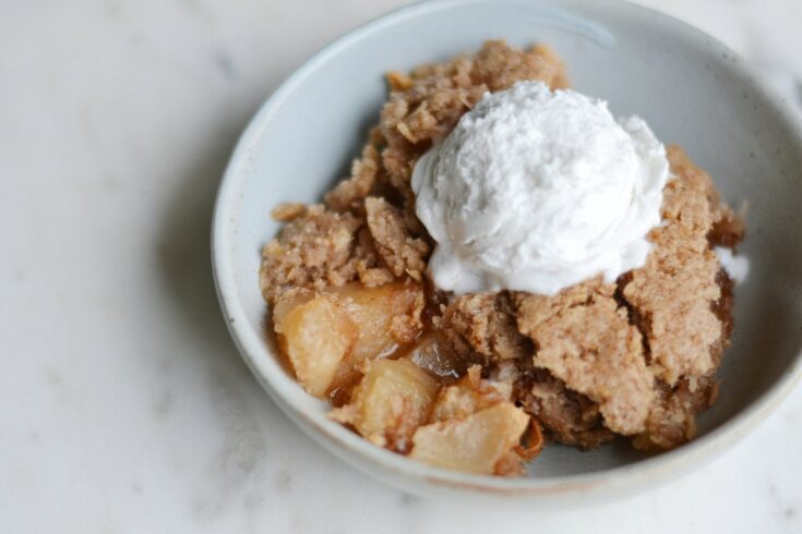 Sweet apple cobbler topped with a scoop of vanilla ice cream, served in a white bowl, perfect for comforting dessert and home baking.