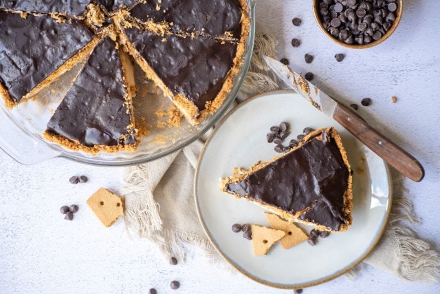 Rich chocolate-covered peanut butter pie sliced into servings on a white plate, with chocolate chips and cookies surrounding it. Perfect for dessert lovers and sweet tooth cravings.