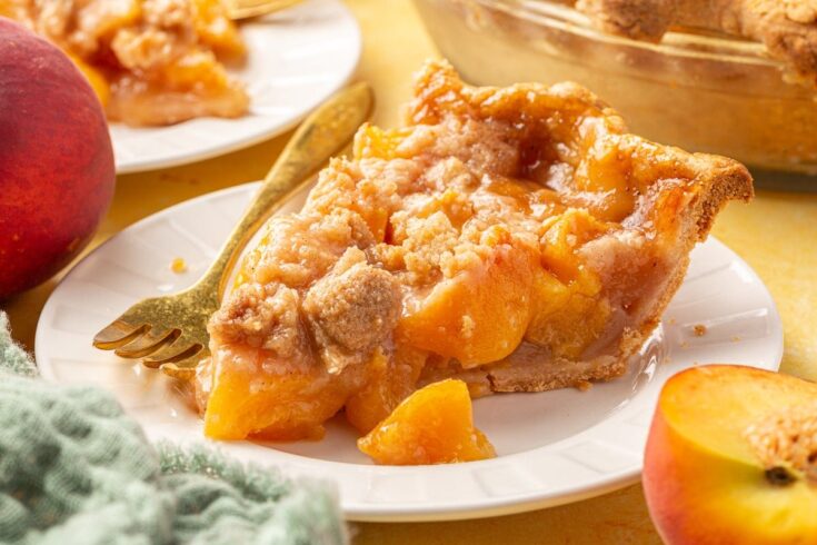 Sweet peach peach cobbler with a golden flaky crust, served on a white plate with fresh peaches and a vintage fork, perfect for comforting summer desserts and homemade baked goods.
