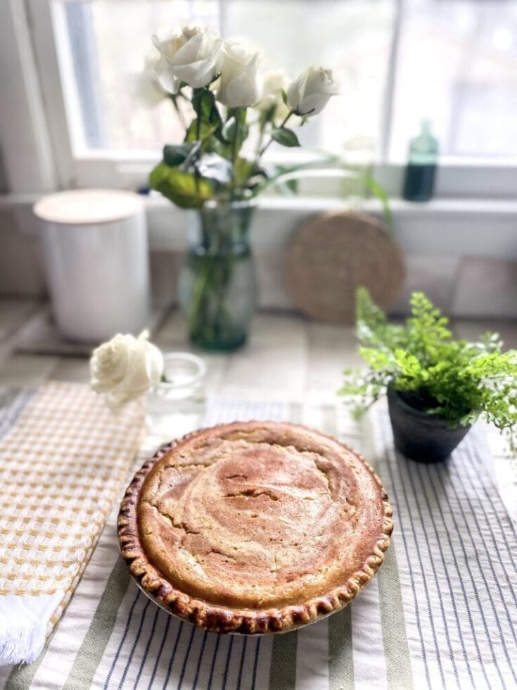 Handmade apple pie on striped cloth table runner, white roses in glass vase, green plant in small pot, cozy kitchen windowsill, soft natural light, warm inviting atmosphere, fresh baked dessert, home baking, comfort food, sweet treats, rustic kitchen decor, A Hundred Affections.