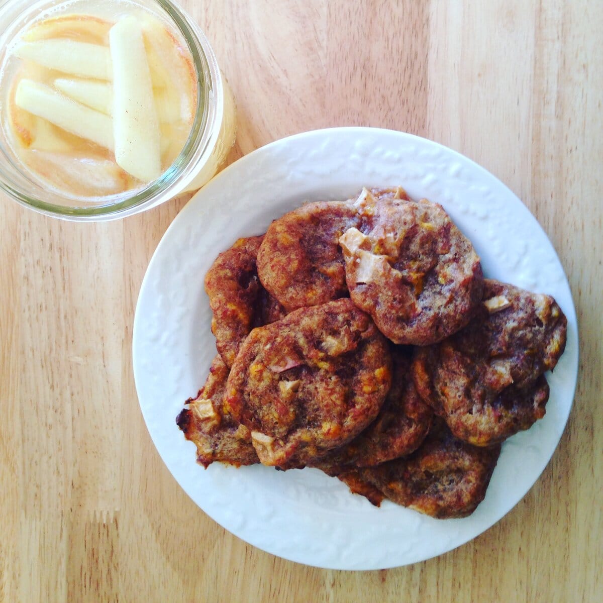 Crispy fried chicken patties served on a white plate with a side of pickled vegetables in a glass jar, on a wooden surface.