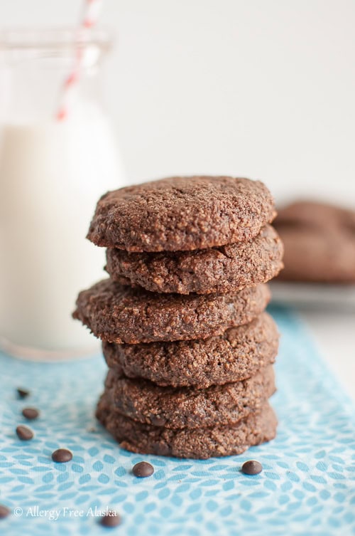 Chocolate cookies stacked in a neat pile, with a glass of milk in the background, perfect for milk and cookie snacking.