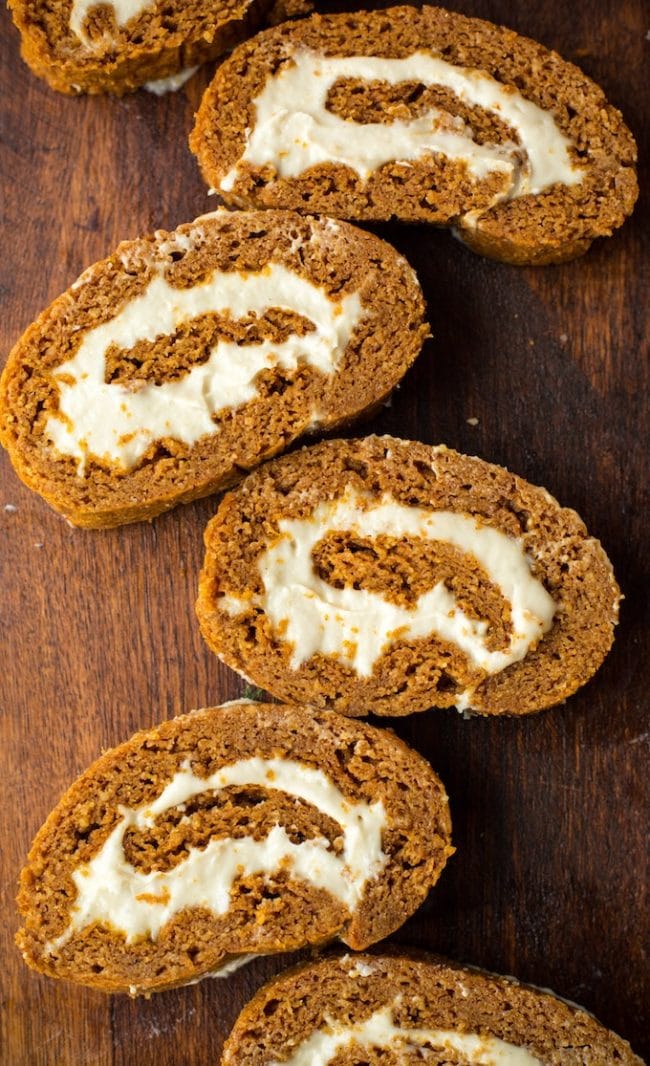 Homemade carrot cake roll slices with cream cheese filling, on a wooden surface, showcasing a moist, spiced dessert perfect for special occasions or everyday indulgence.