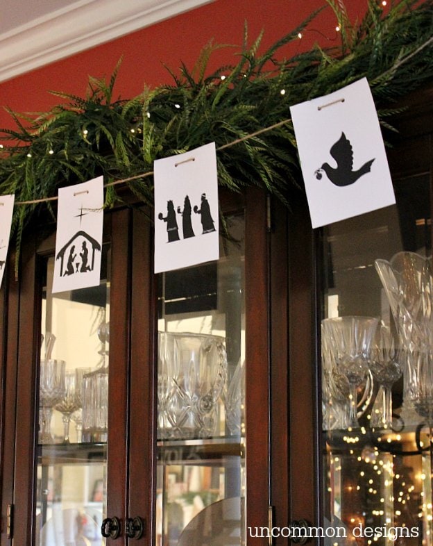 Silhouette nativity and angel paper decorations hanging above a glass cabinet with crystal glassware. Perfect for Christmas or religious holiday decor, creating a festive and meaningful atmosphere.