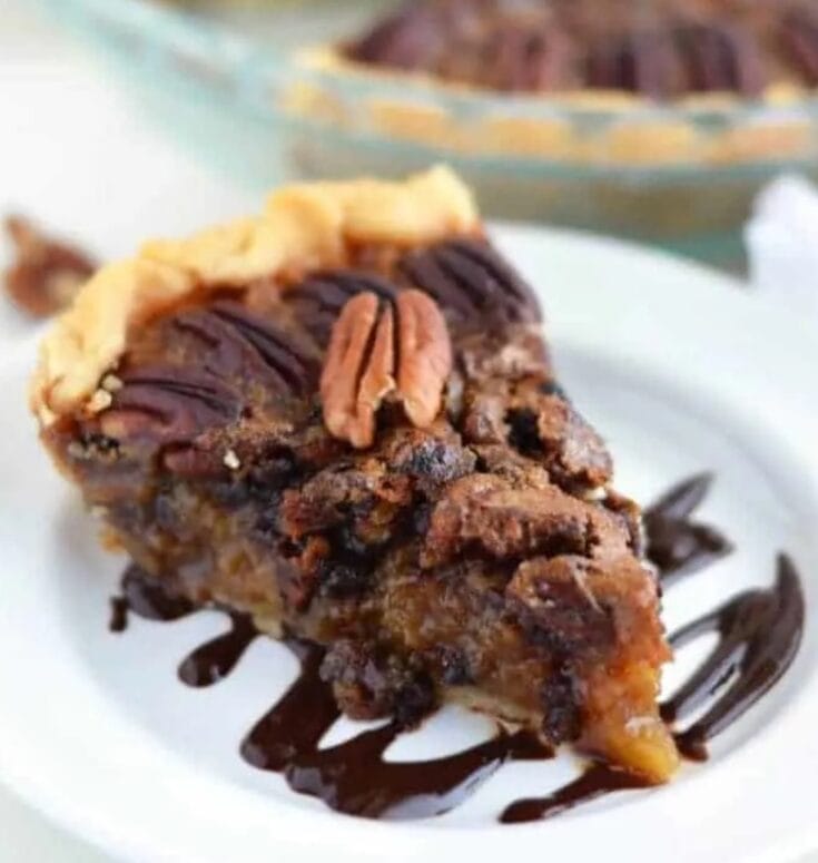 Rich chocolate pecan pie slice with caramelized pecans, drizzled with chocolate sauce, served on a white plate. Perfect for dessert lovers and pie enthusiasts.