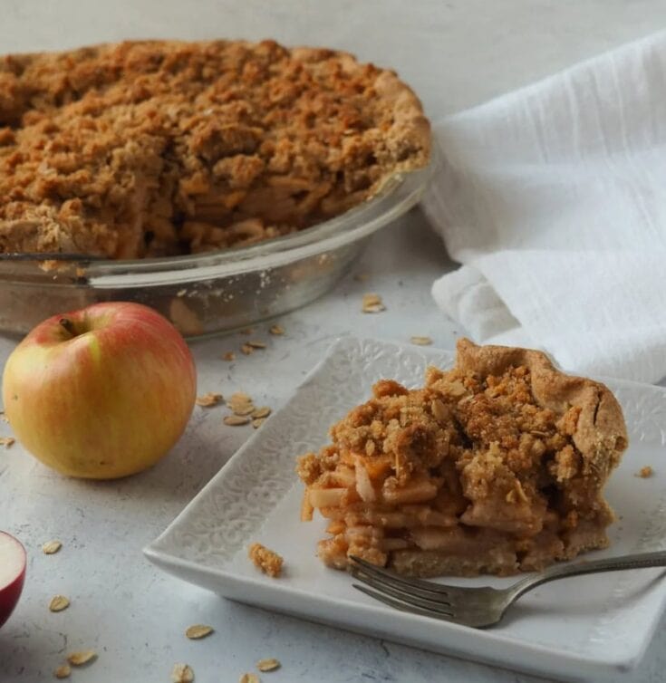 Golden apple with homemade apple crumble pie with crumbly topping on a white plate and a fork.