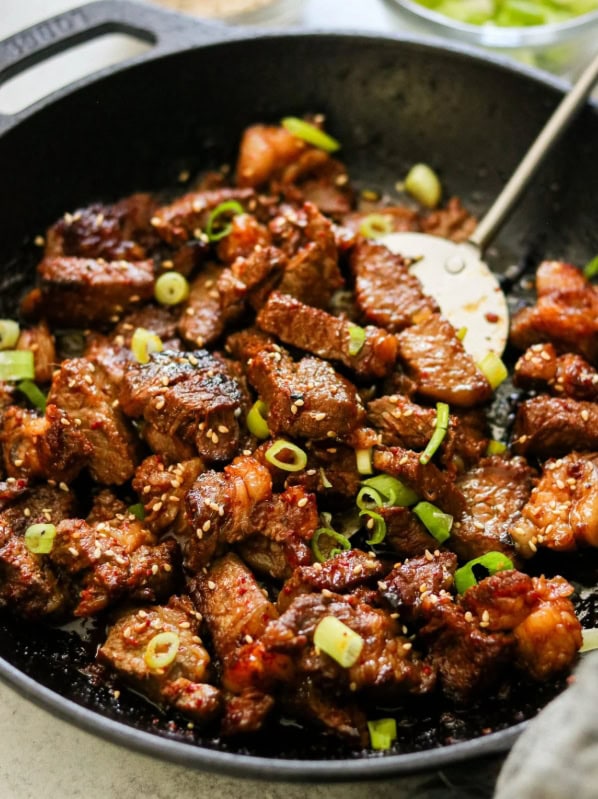 Juicy, flavorful stir-fried beef with green onions and sesame seeds in a black skillet, perfect for easy Asian-inspired meals and outdoor dining.