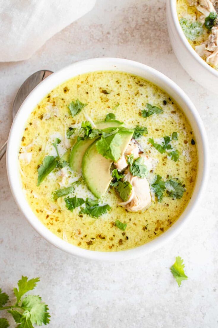 Creamy chicken and green chile soup garnished with avocado slices and fresh cilantro in a white bowl. Perfect for comforting home-cooked meals and exploring flavorful soup recipes.