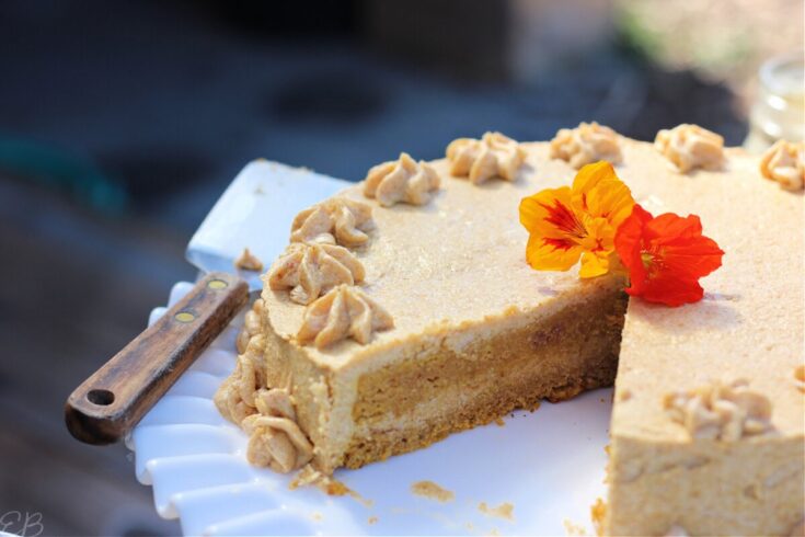 Sweet potato cake with peanut butter frosting on a white cake stand with edible flowers, perfect for a dessert recipe or special occasion celebration.