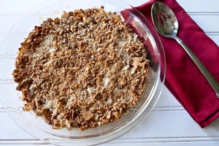 Crumbled apple crisp dessert in a glass baking dish with a golden brown topping, served with a silver spoon on a red napkin, perfect for cozy fall comfort food recipes, from A Hundred Affections.