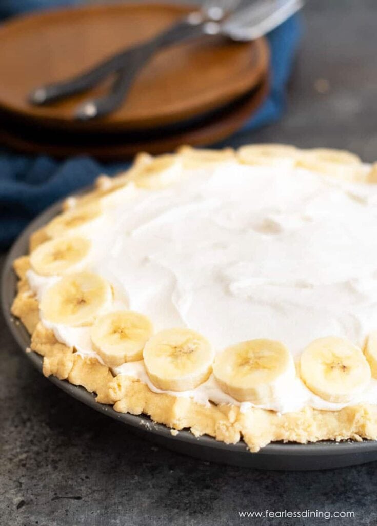 Banana cream pie with a flaky crust, fresh sliced bananas, and whipped cream on top, served on a dark plate; ideal for dessert or special occasions.