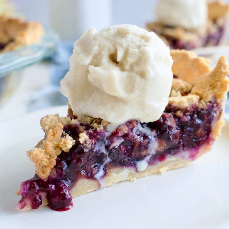 Fresh homemade mixed berry pie with a scoop of vanilla ice cream on top, highlighted by a flaky golden crust and sweet, juicy berry filling, perfect for dessert lovers.