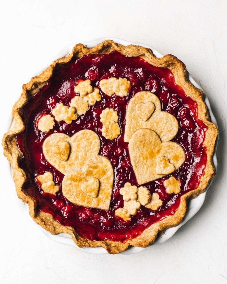 Fresh raspberry pie with heart-shaped and flower-shaped cookie toppings, showcasing rustic and homemade dessert aesthetic, ideal for Valentine's Day or romantic occasions.