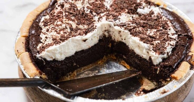 Rich and decadent chocolate cream pie with whipped topping and chocolate shavings, served in a pie dish with a slice removed, perfect for dessert lovers.