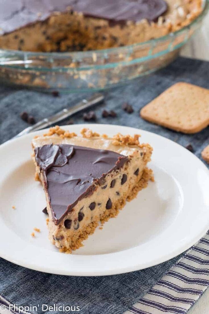 Rich chocolate chip cookie dough cheesecake with a chocolate ganache topping, baked in a glass dish, served on a white plate with a side of cookies, perfect for dessert lovers.