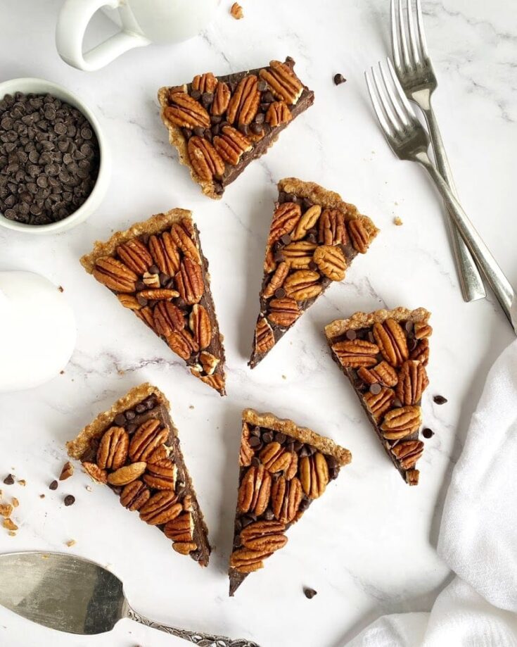 Rich chocolate pecan pie bars with gooey filling, topped with toasted pecans, served on a white marble surface. Perfect for holiday desserts or special occasions.