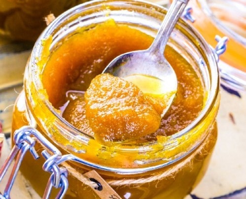 Creamy homemade peach jam in a glass jar with a metal clasp, ready to spread or use in recipes, showcasing fresh, sweet, and natural fruit preserves.