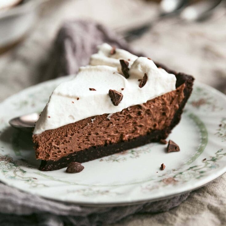 Rich chocolate pie with whipped cream and chocolate chunks on vintage floral plate for A Hundred Affections dessert recipe blog.