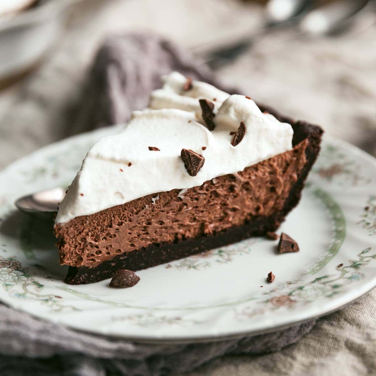 Rich chocolate pie with whipped cream and chocolate chunks on vintage floral plate for A Hundred Affections dessert recipe blog.