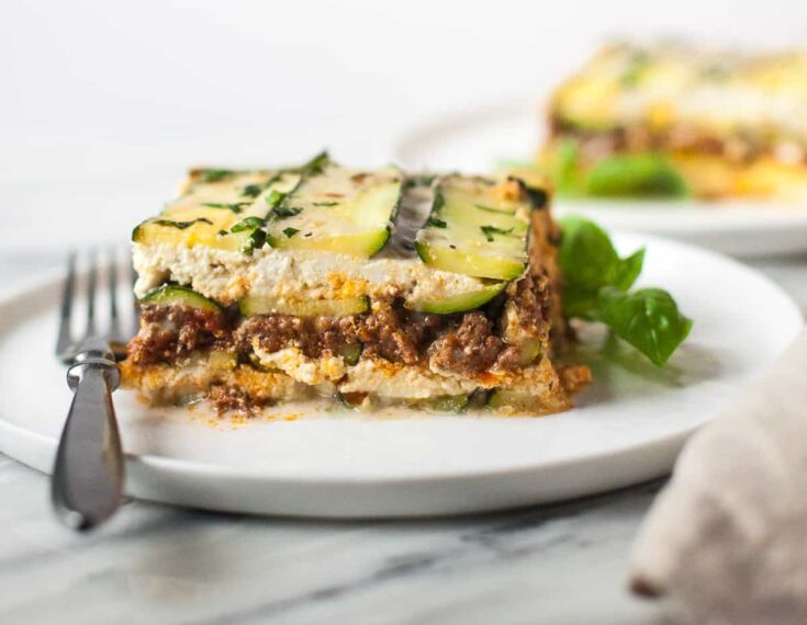 Layers of zucchini, meat sauce, and creamy ricotta cheese in a healthy zucchini lasagna dish served on a white plate.