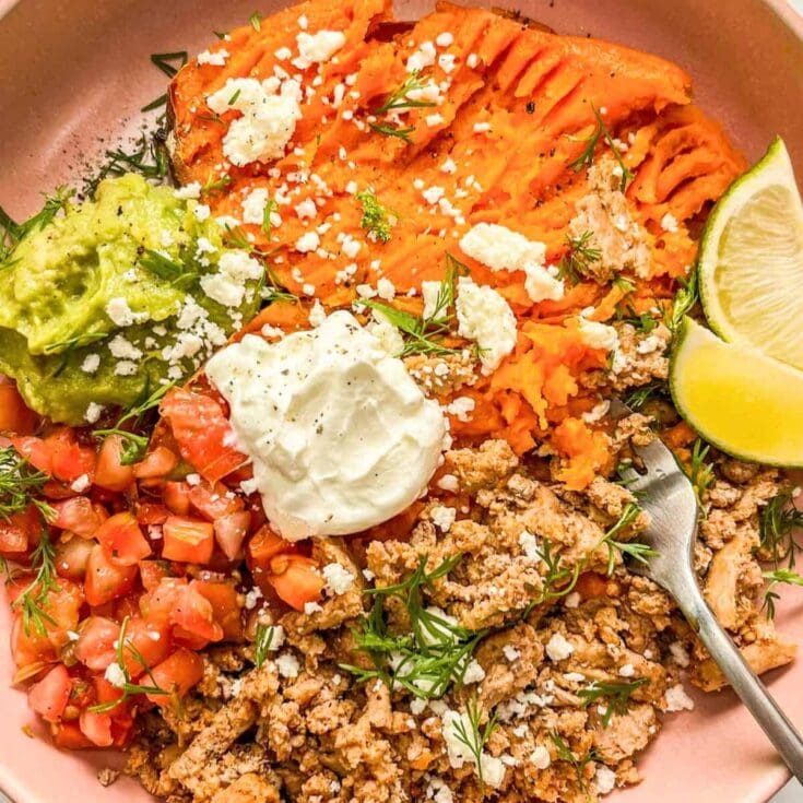Roasted sweet potatoes with feta and herbs, fresh avocado and tomato salad, lime wedges, and seasoned ground turkey in a pink bowl for healthy meal inspiration.